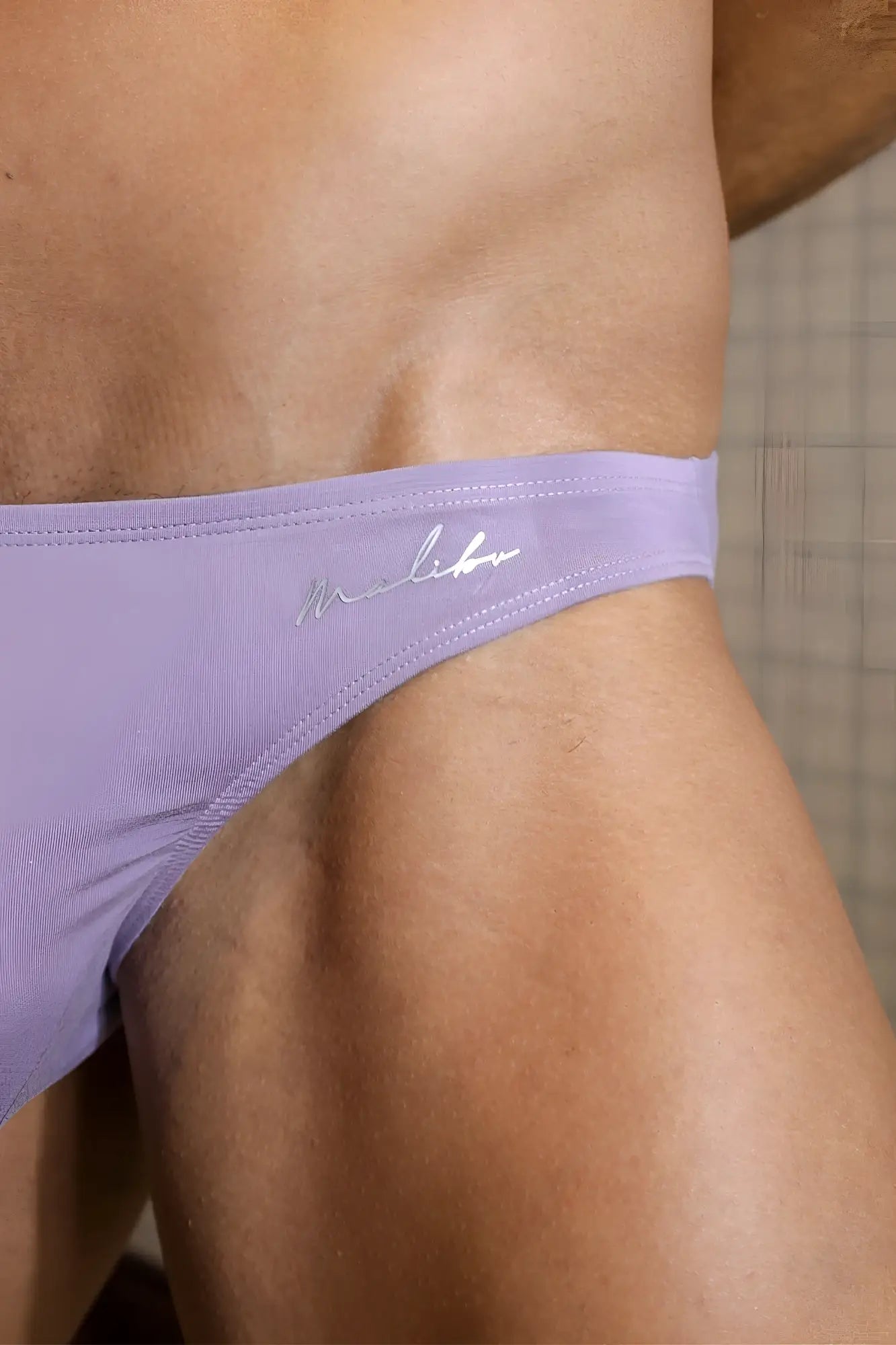 Lavender-colored premium modal scrunch-back cheeky briefs with silver embroidered logo on waistband, shown from the back