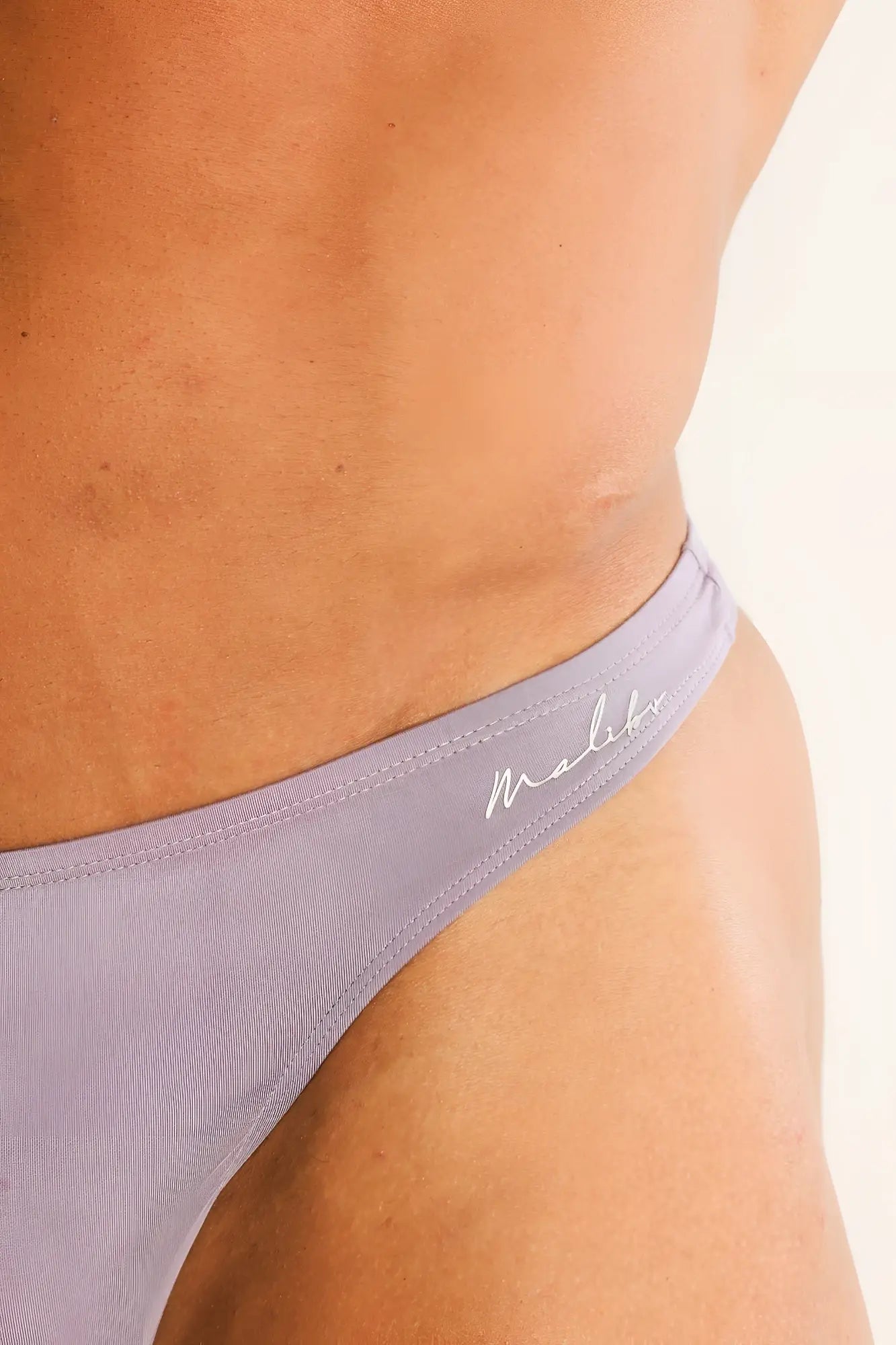 Lavender-colored premium modal scrunch-back thong bikini bottom with textured fabric and white branding on waistband back side