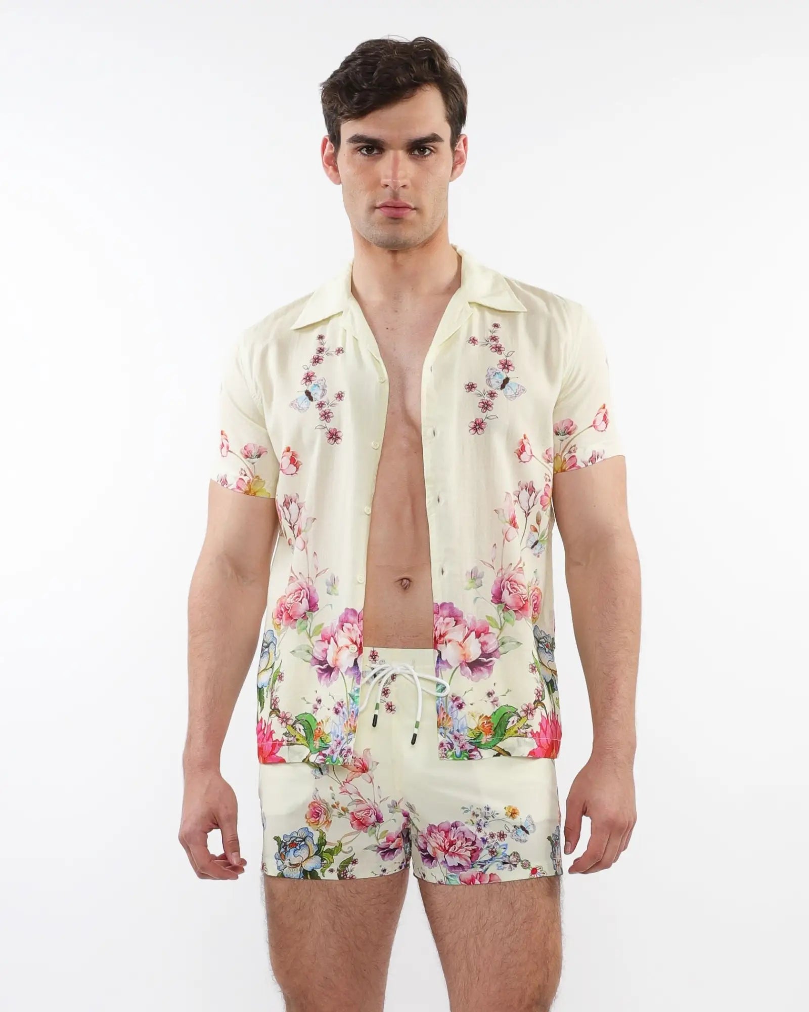 A man wearing a cream printed s s woven modal border shirt and matching floral shorts in pink purple and green colors