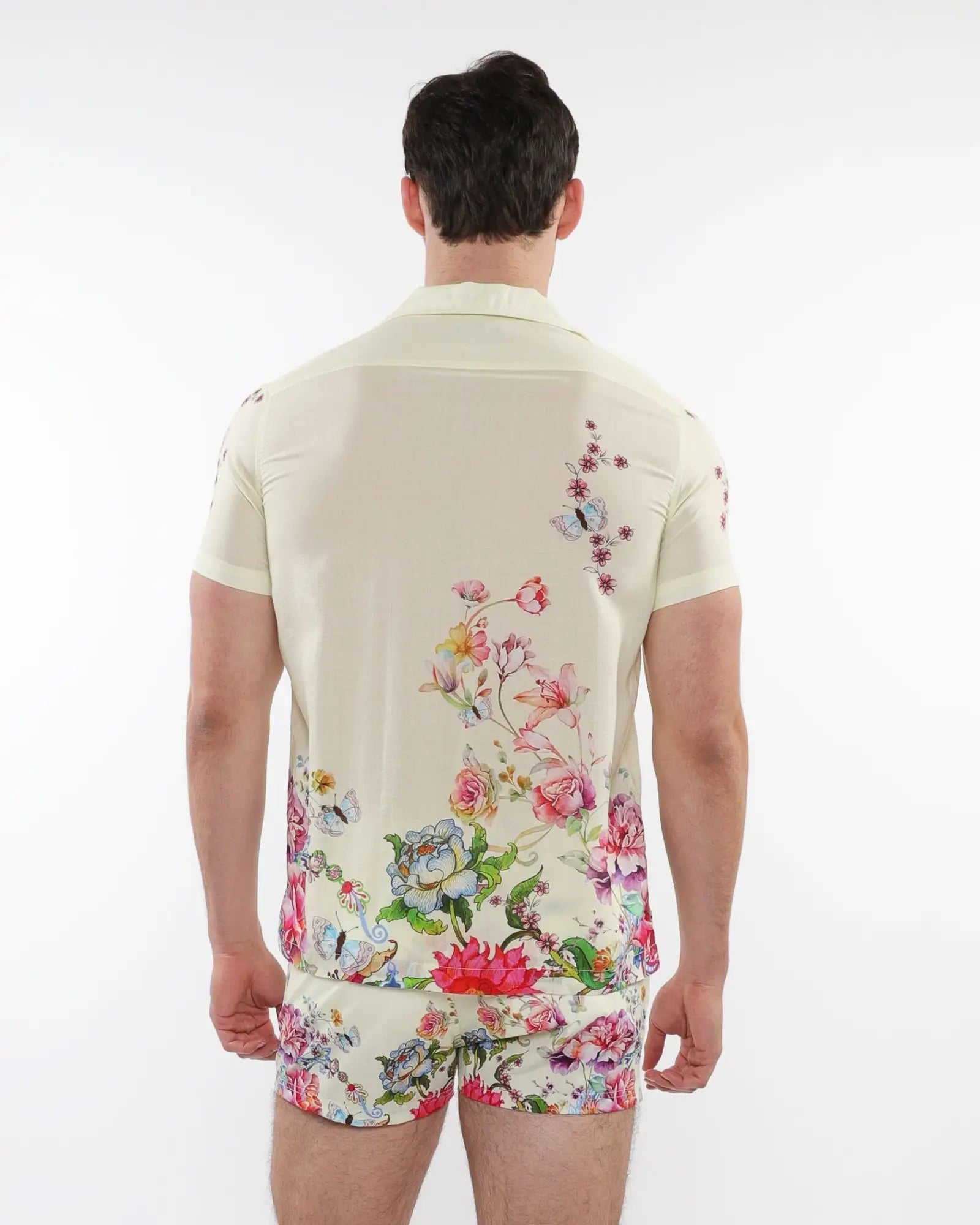 A man wearing a cream-colored printed short-sleeved woven modal border shirt with vibrant floral and butterfly patterns