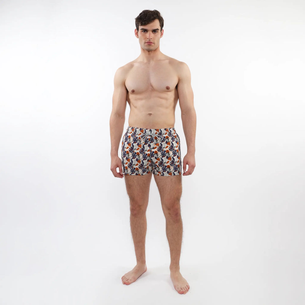 Men’s printed swim shorts with mesh lining featuring vibrant orange navy and white tropical leaf and fruit pattern on light fabric