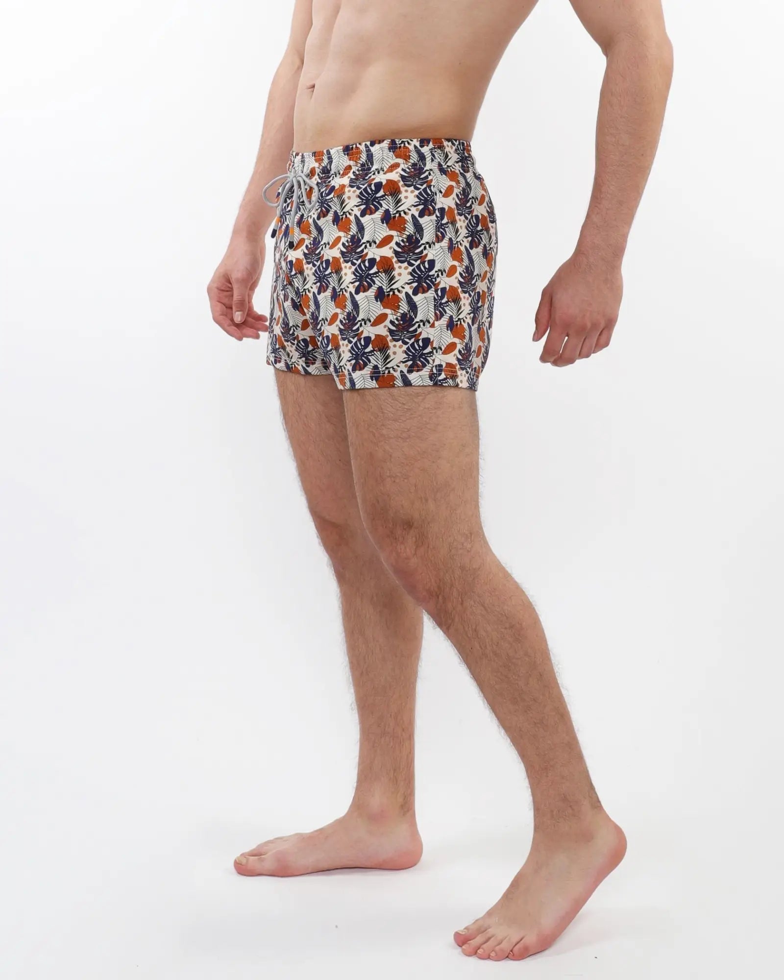 Men’s printed swim shorts with mesh lining featuring vibrant navy orange and cream tropical leaf and fruit pattern on white