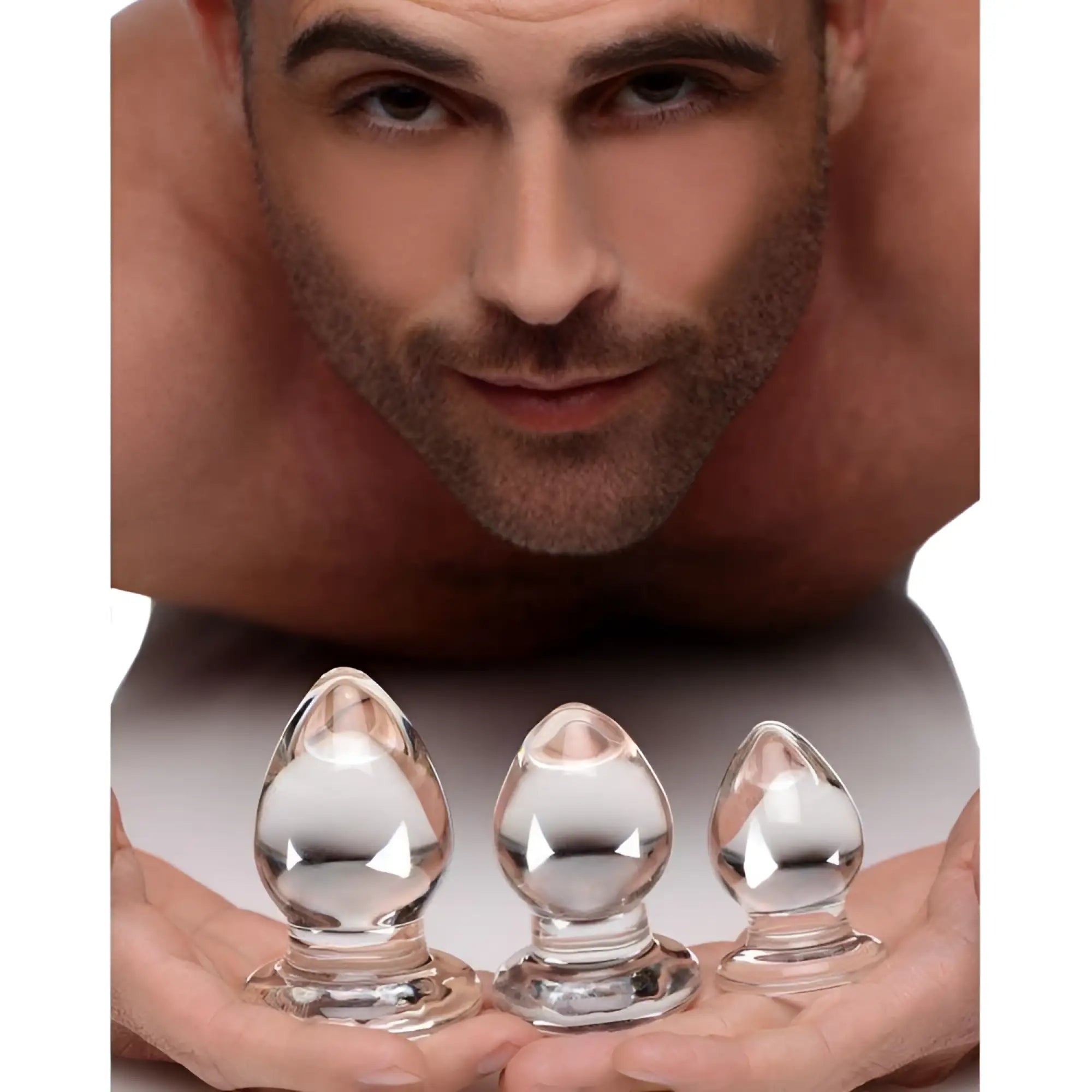 Prisms Erotic Glass 3 Piece Anal Plug Kit: A man holds three clear, graduated glass plugs in his hands.