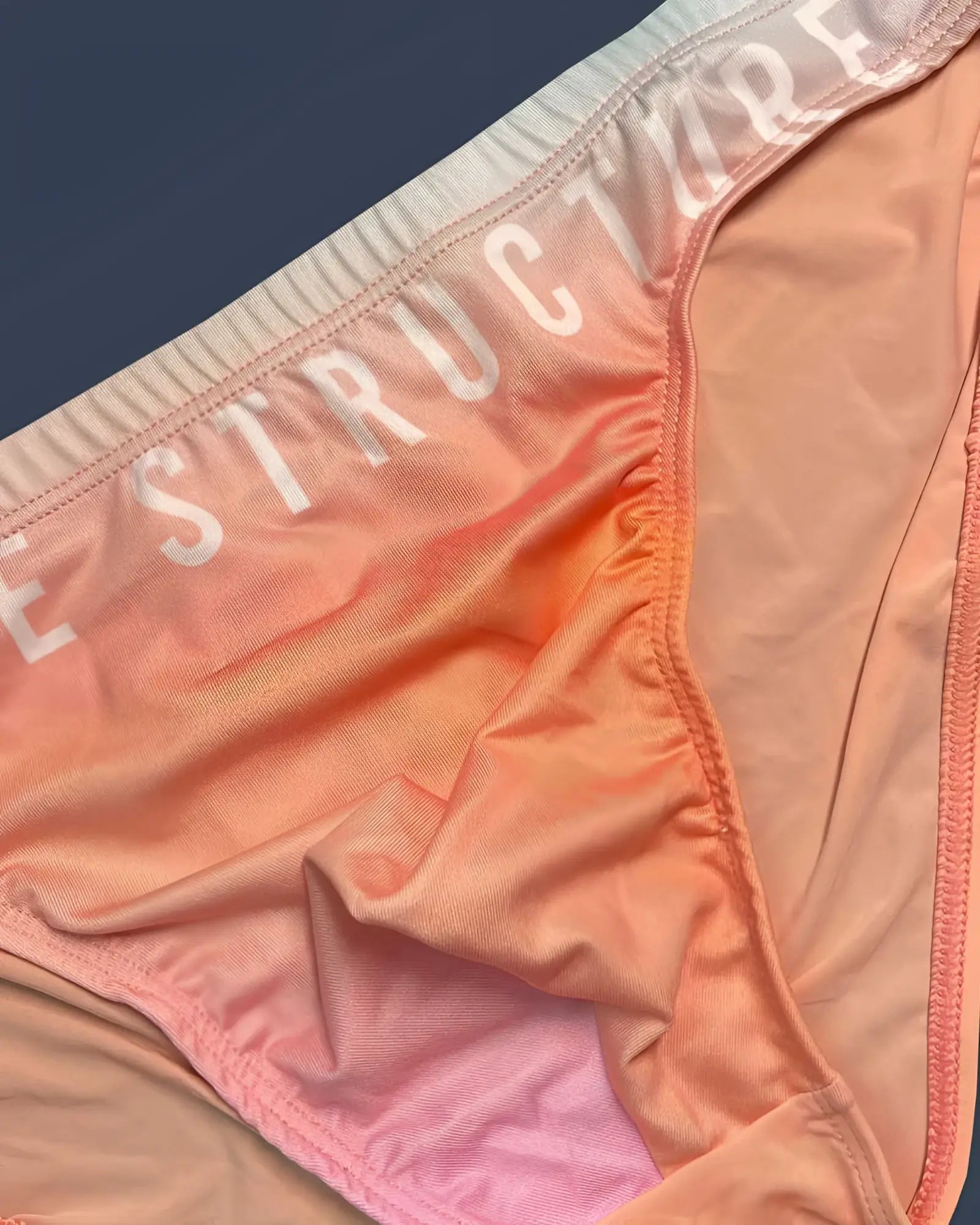 Peach and pink gradient fabric bikini bottom with structure printed in white on waistband by Private Structure in orange