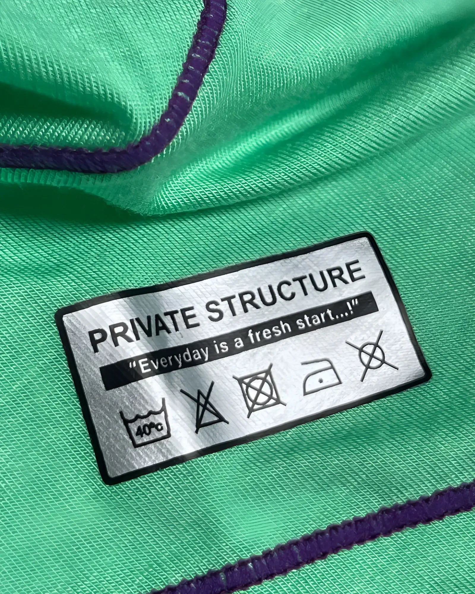 Green fabric with purple stitching and a silver private structure label showing care instructions on prime elysian hipster