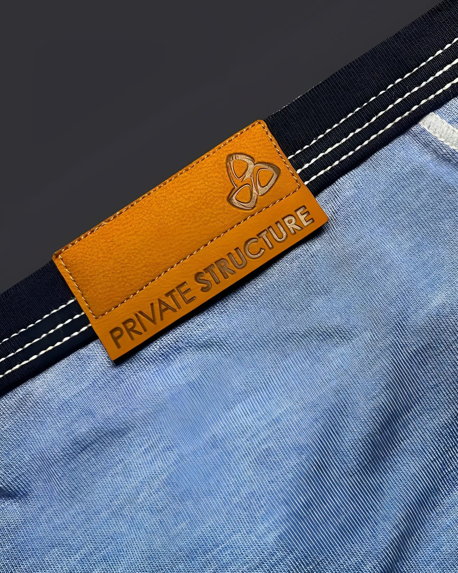 Orange leather brand tag with embossed logo and private structure text on blue denim fabric of mini brief back