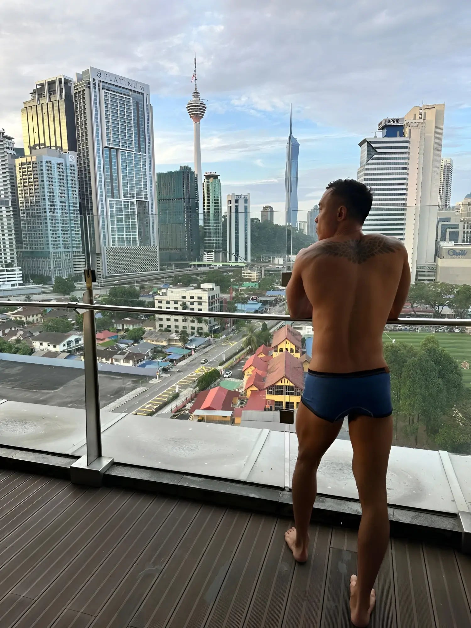 A man stands on a wooden balcony wearing dark blue denim private structure LCUT4359 barn boy low rise trunks