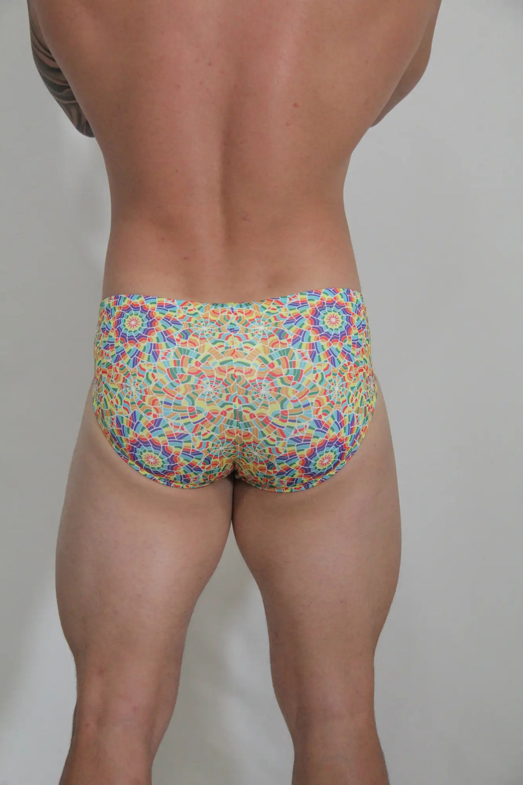 Vibrant rainbow kaleidoscope swim brief with multicolored mosaic pattern and bold geometric design