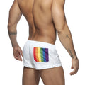 White swim trunks with a vibrant rainbow flag patch on the back pocket shown from the back side