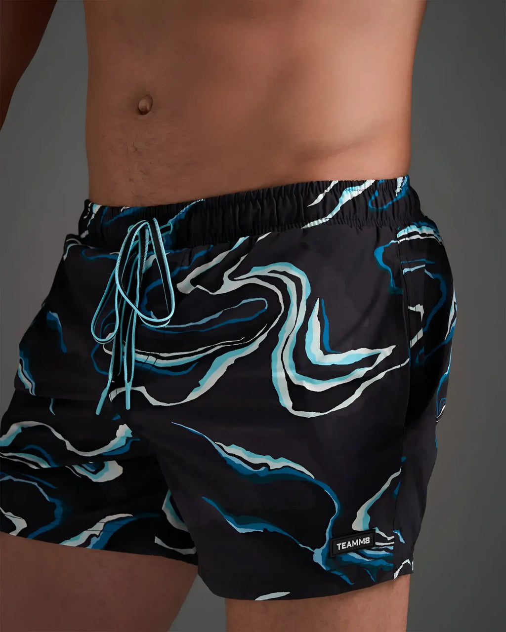 Black resort swim short with dynamic blue and white swirl pattern and light blue drawstrings for beachwear