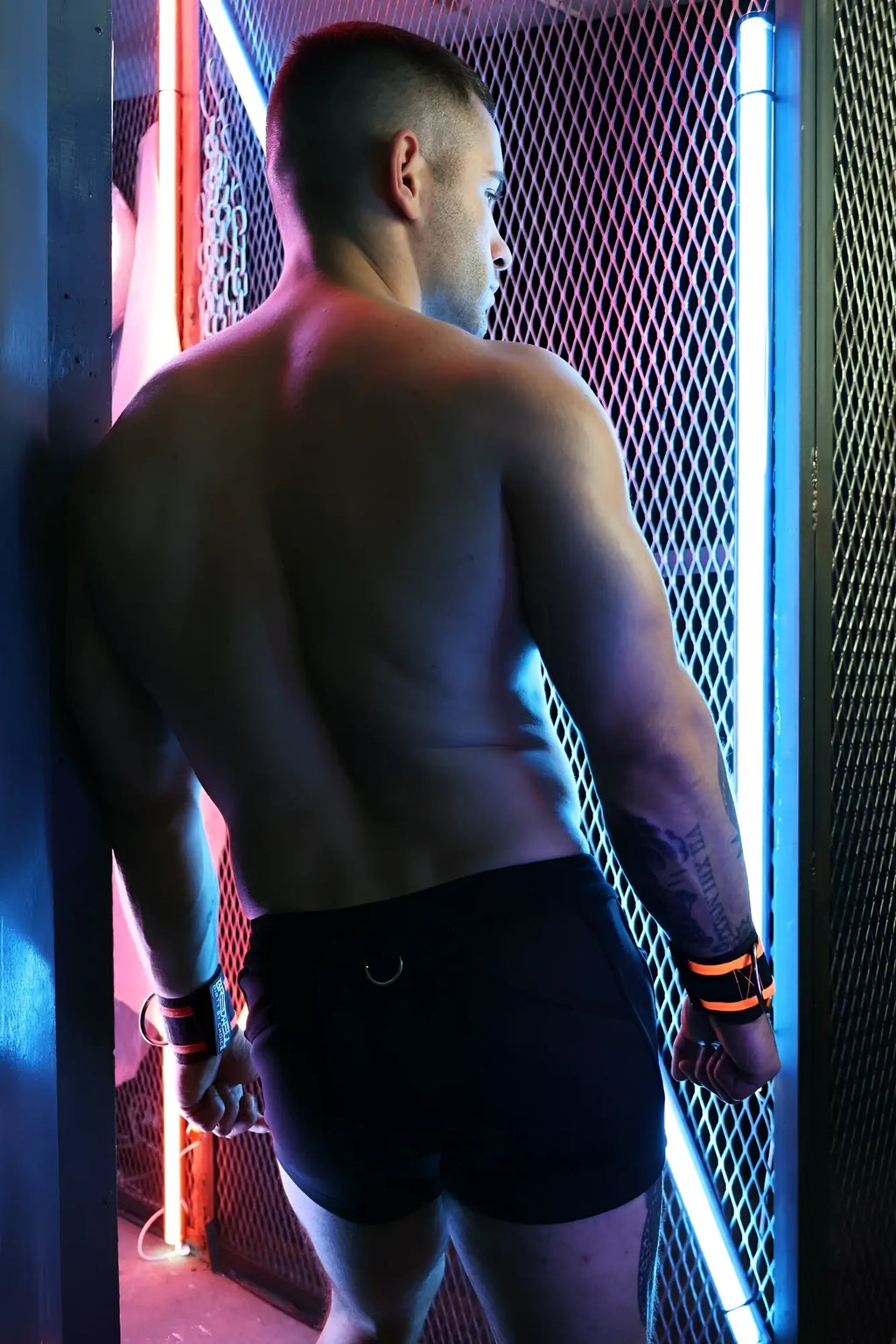 A muscular man wearing black revolution shorts with orange wristbands showcasing the front view of the product