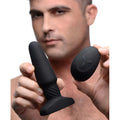 A man holds a smooth, black Rimmers Slim R rimming plug and its matching pebble-shaped remote control.