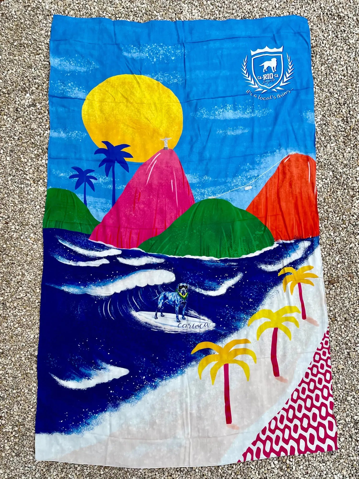 A vibrant Rio Aquarela canga de praia beach towel with colorful surf scene and dog surfing on waves in bright colors