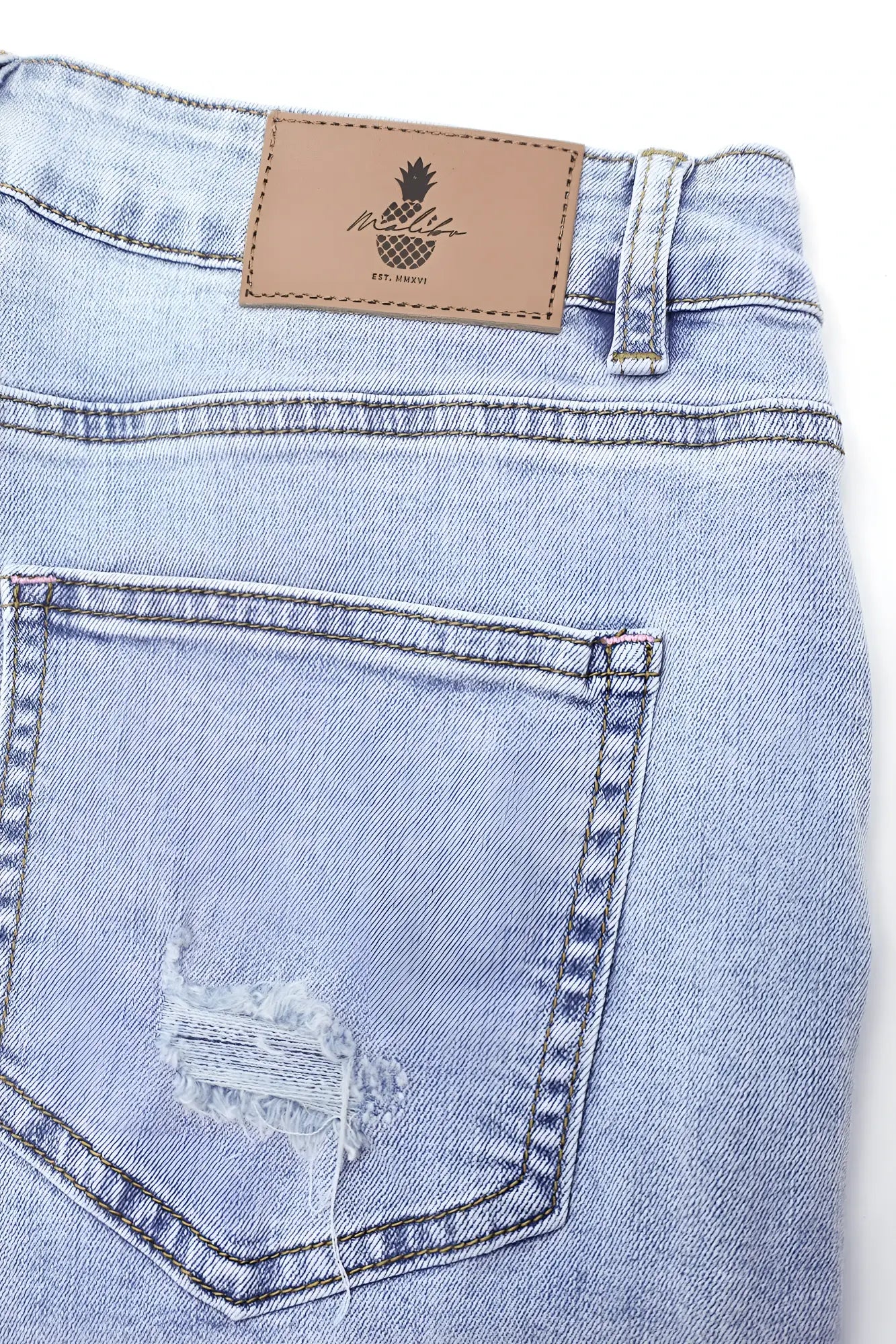 Back of rockstar raw cut 2.5 inch denim short shorts in capri blue with distressed pocket and pineapple leather patch