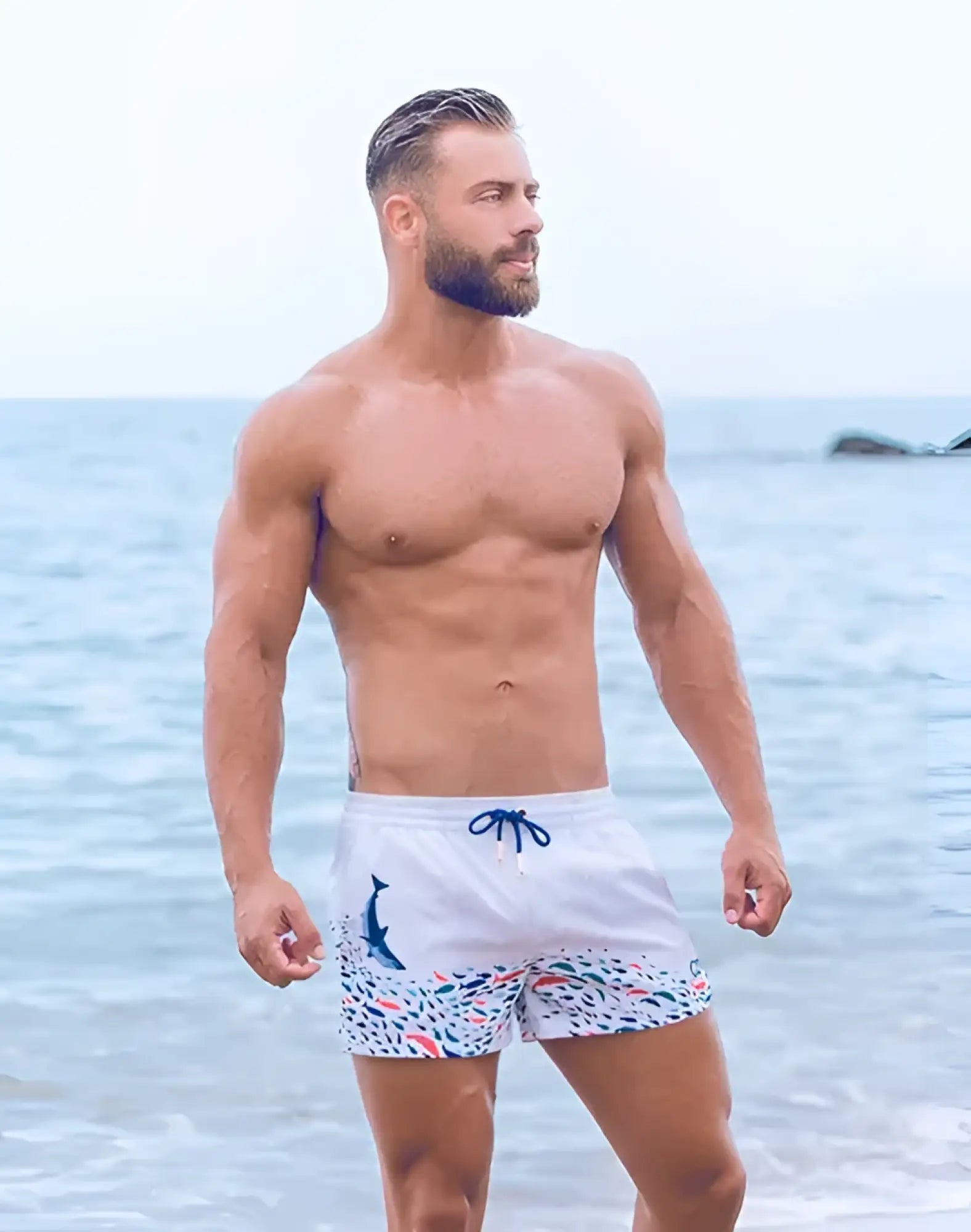 White swim trunks featuring a blue dolphin graphic and colorful fish pattern with navy drawstrings for beachwear