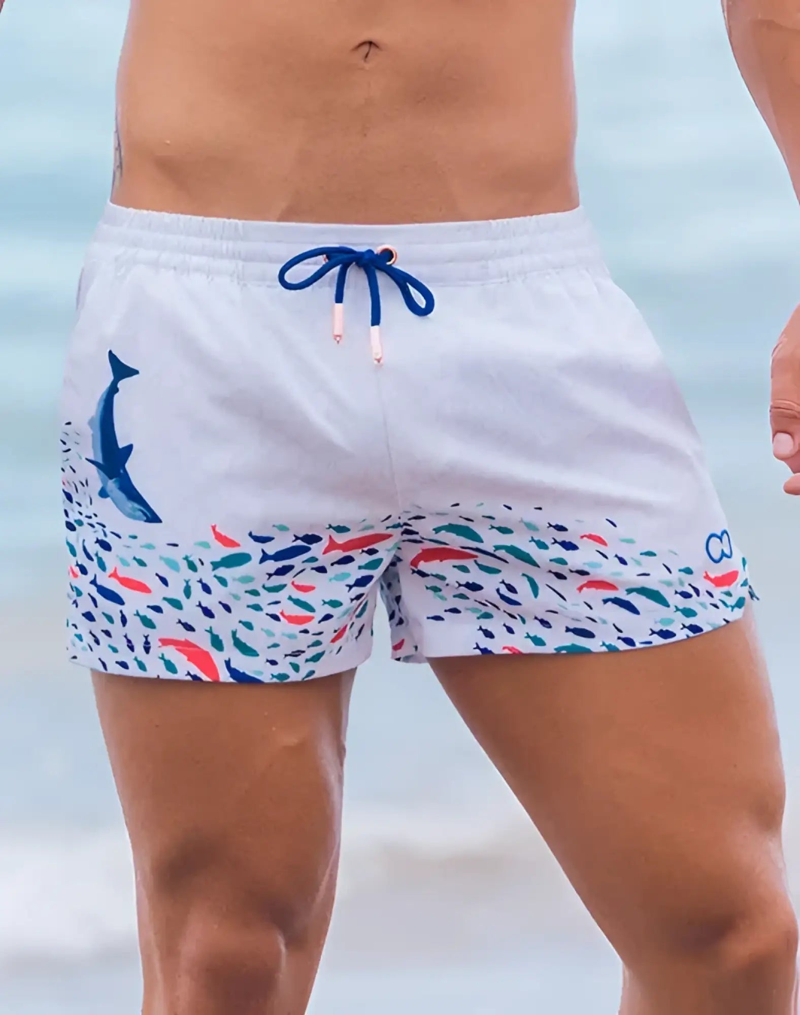 White swim trunks with vibrant underwater print featuring a blue dolphin and multicolored fish with navy drawstrings