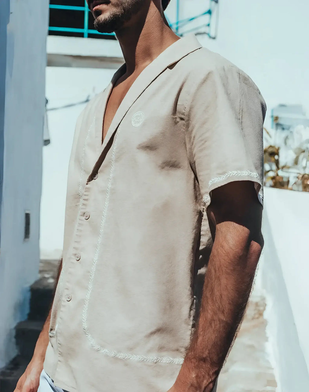 Beige santorini linen shirt with short sleeves and white embroidered trim along placket and sleeve cuffs