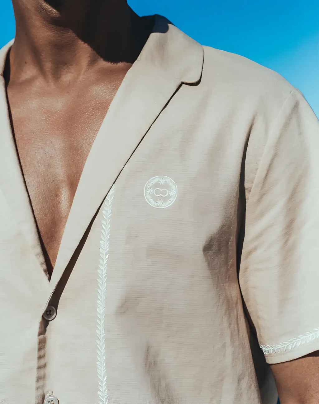 Beige Santorini linen short-sleeved shirt with white embroidered detailing and circular logo on the chest