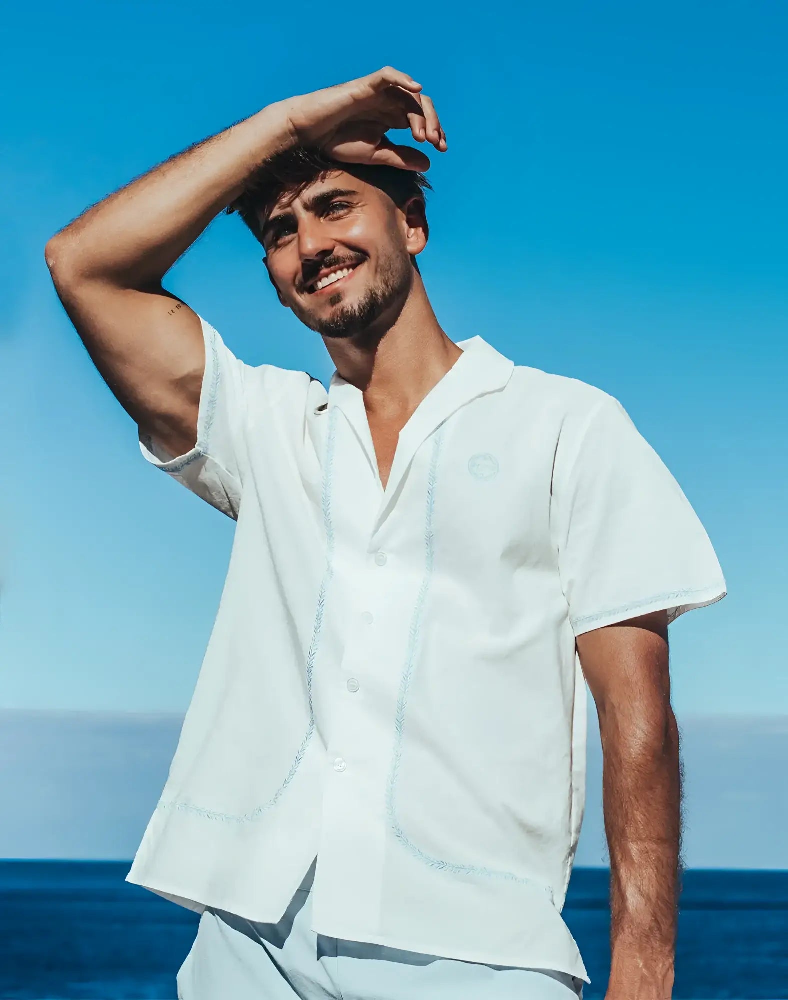 White Santorini linen short-sleeved shirt with light blue embroidery and a small circular logo on the left chest