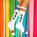 White crew socks with black say gay lettering and rainbow striped cuffs toe caps and heels knee high style