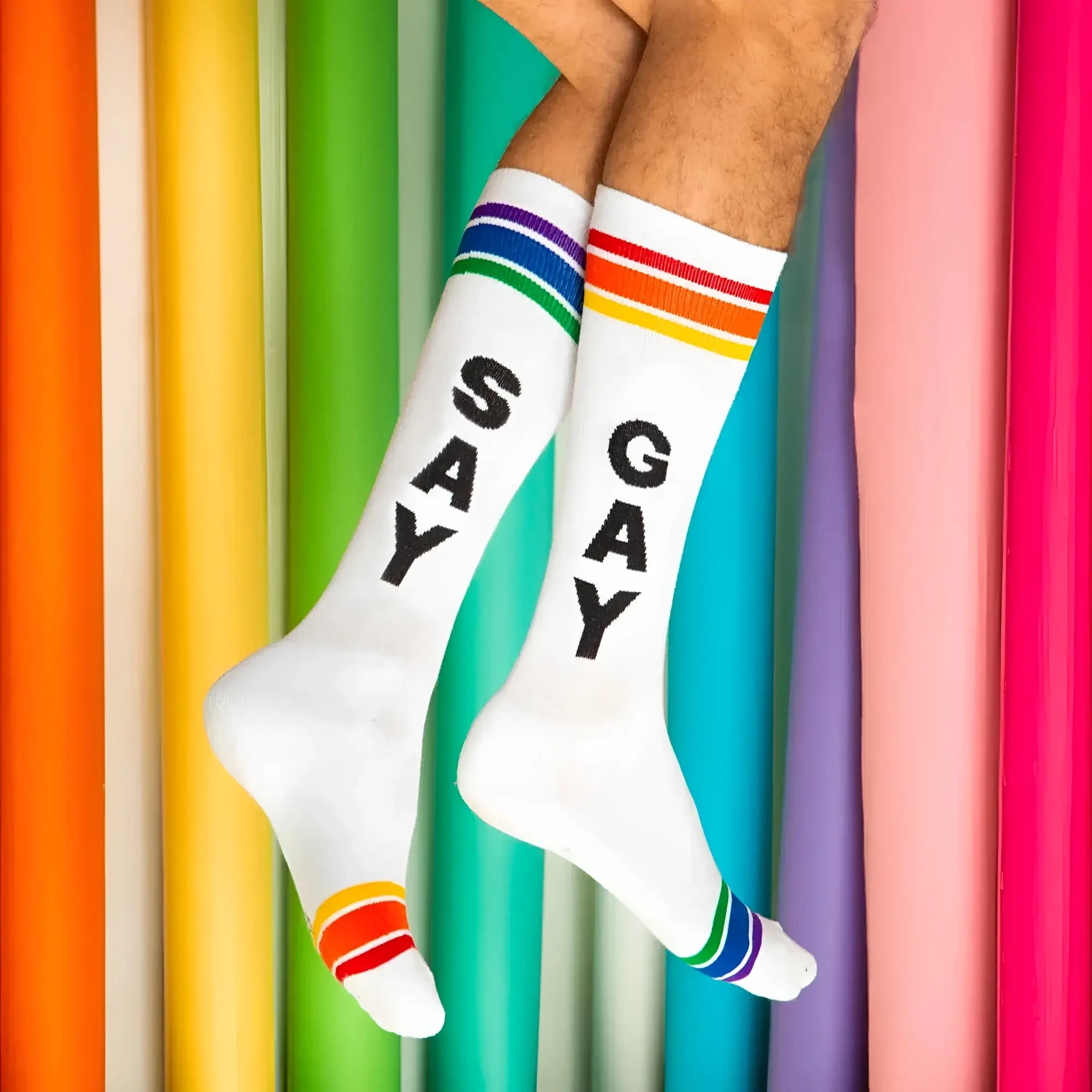 White crew socks with black say gay lettering and rainbow striped cuffs toe caps and heels knee high style