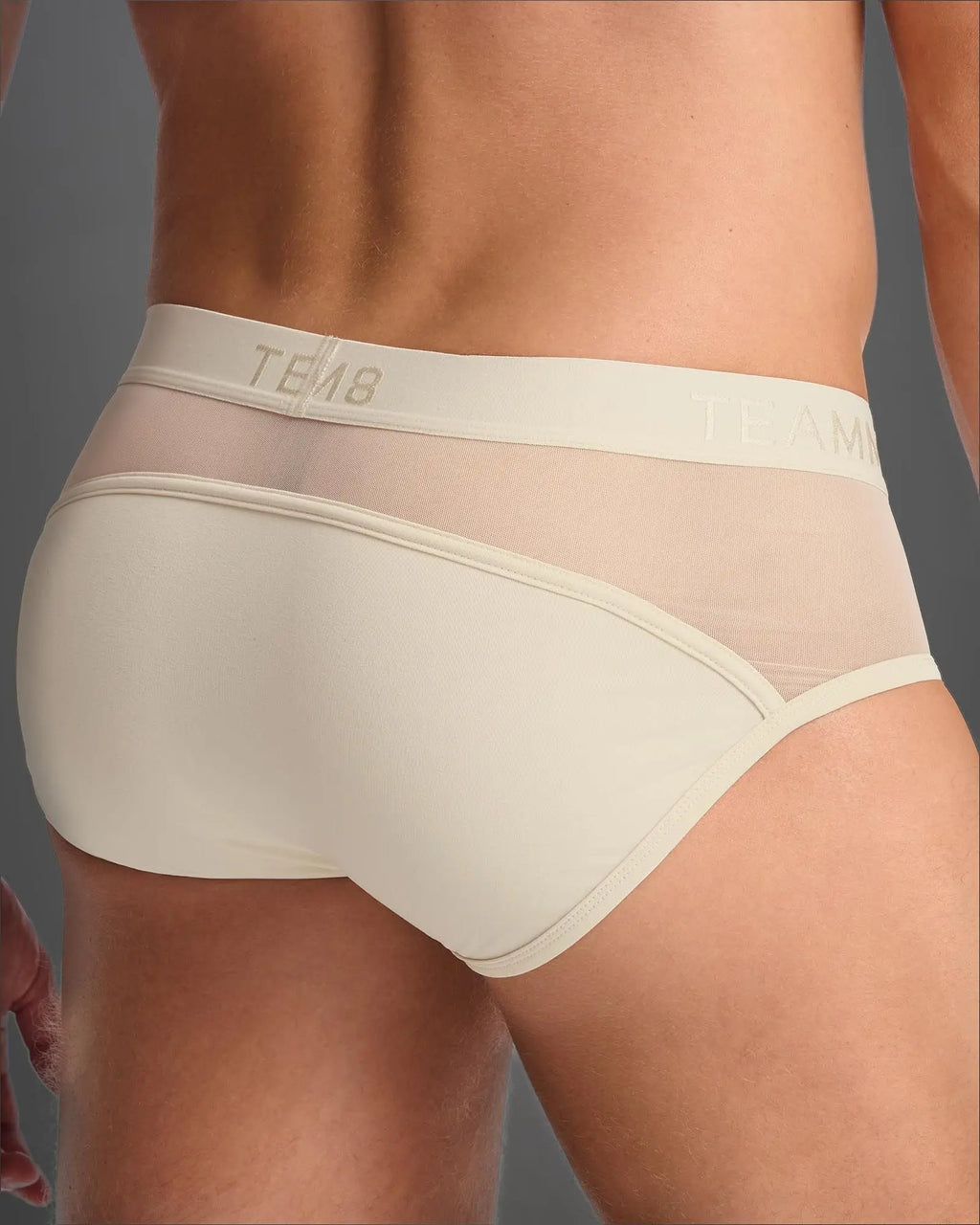 Cream-colored score sheer brief with sheer mesh front, solid back panel, and elastic waistband with tem8 logo