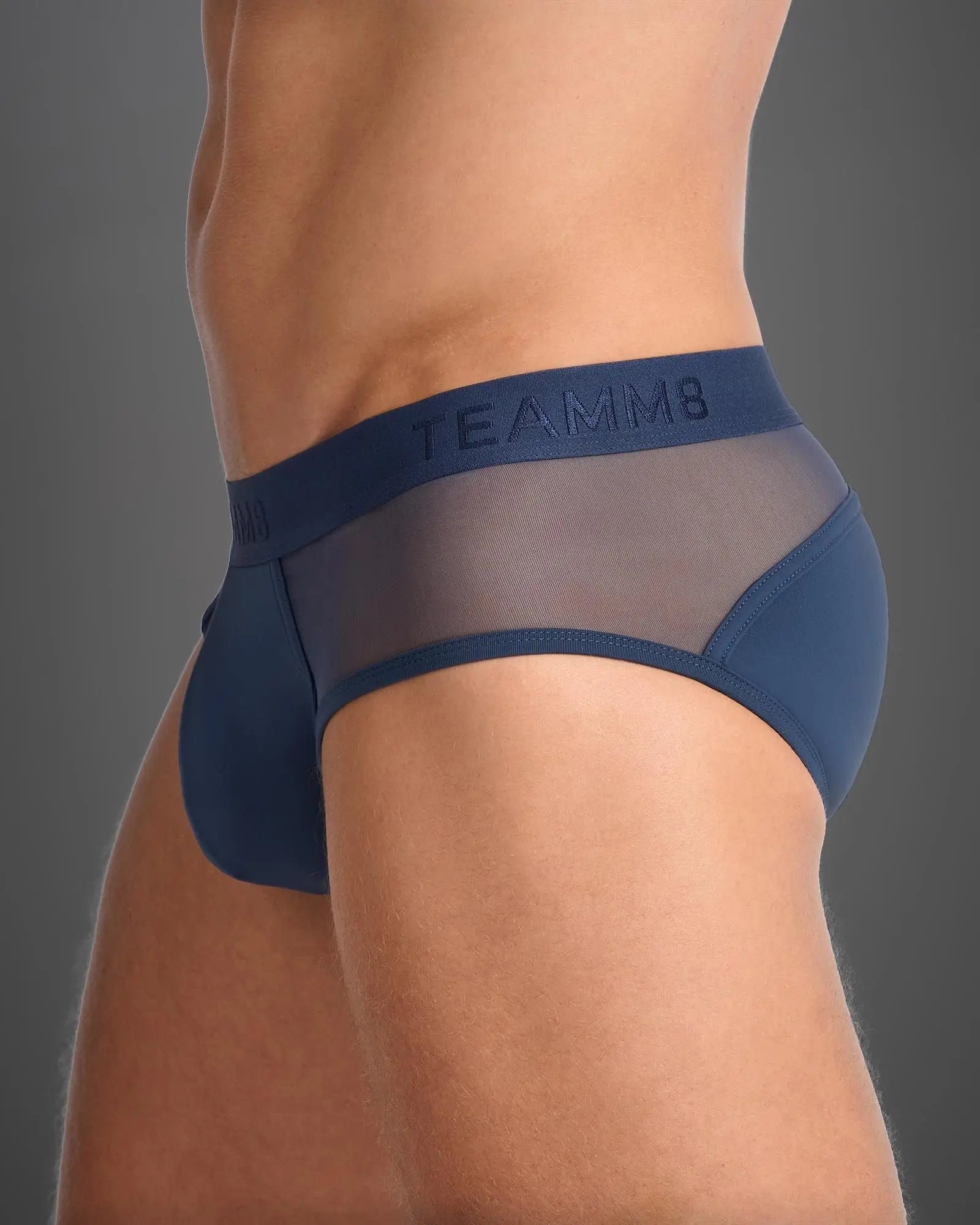 Navy blue team8 men’s score sheer brief with sheer mesh panels and a branded waistband shown from the back side