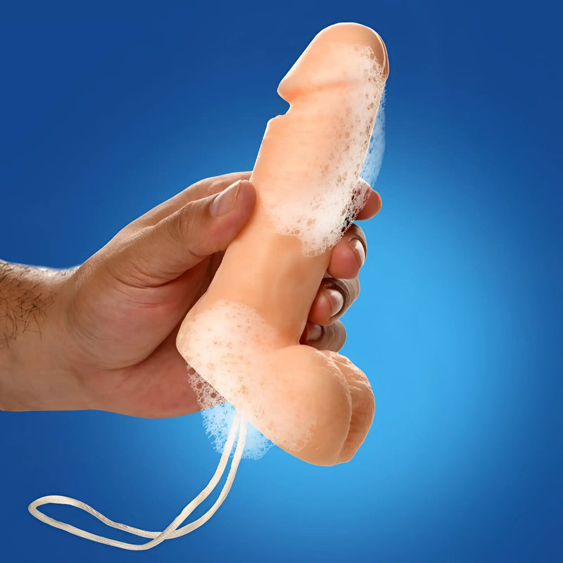 A hand holds a soapy, beige phallus-shaped Sex on a Rope Pecker Soap with a white hanging cord against a blue background.