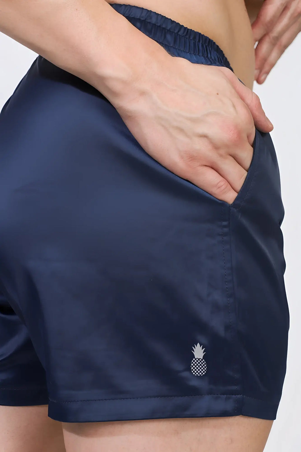 Navy shimmerflex active shorts made of satin with a white pineapple logo embroidered on the lower right leg