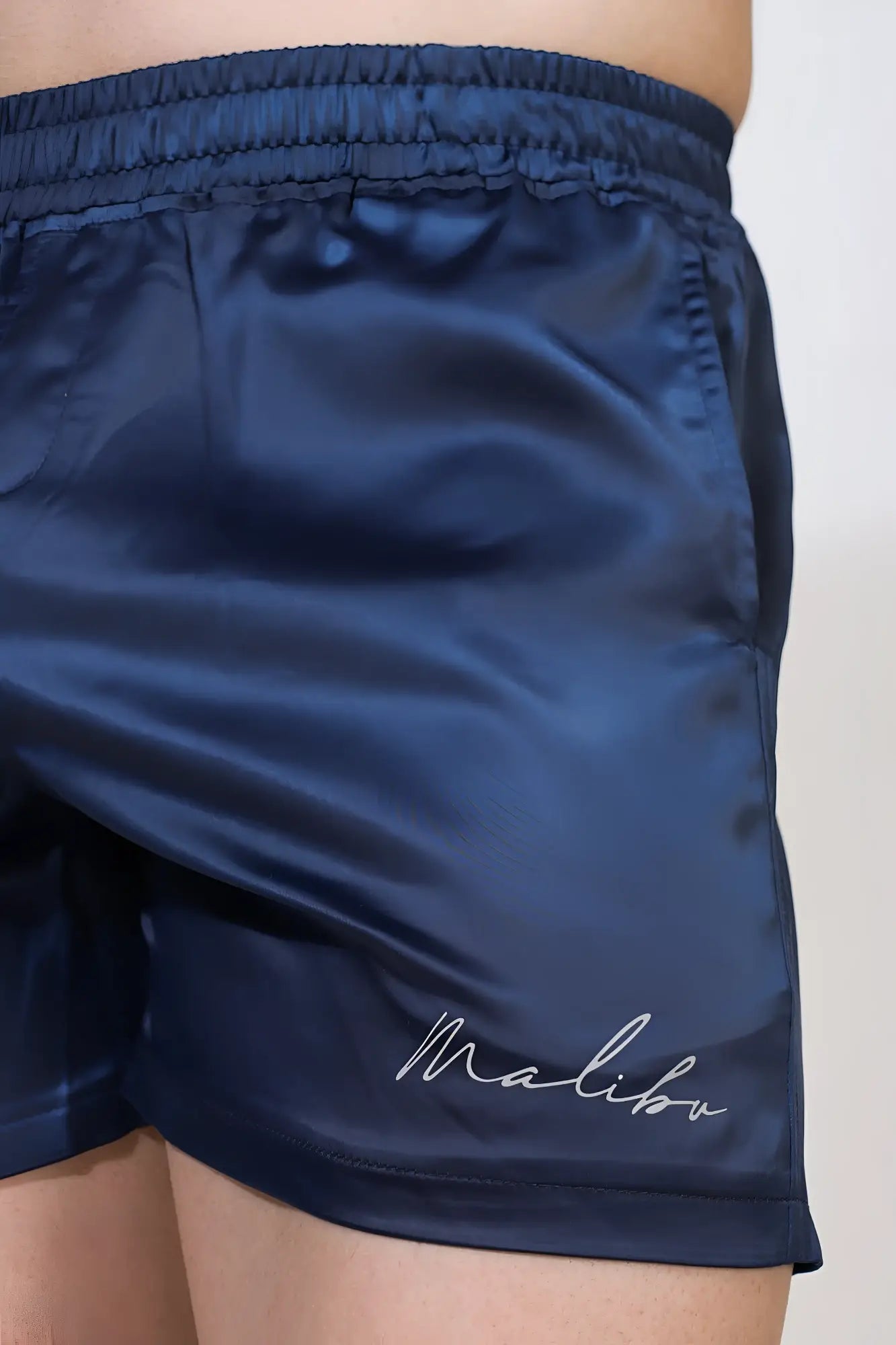 Navy shimmerflex active shorts in satin featuring a white cursive malibu logo embroidered on the lower leg