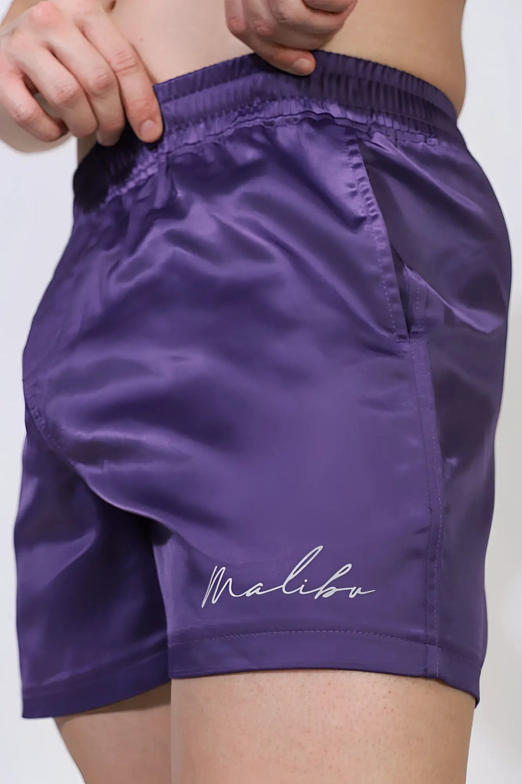 Purple satin shimmerflex active shorts with white malibu logo embroidered on lower leg