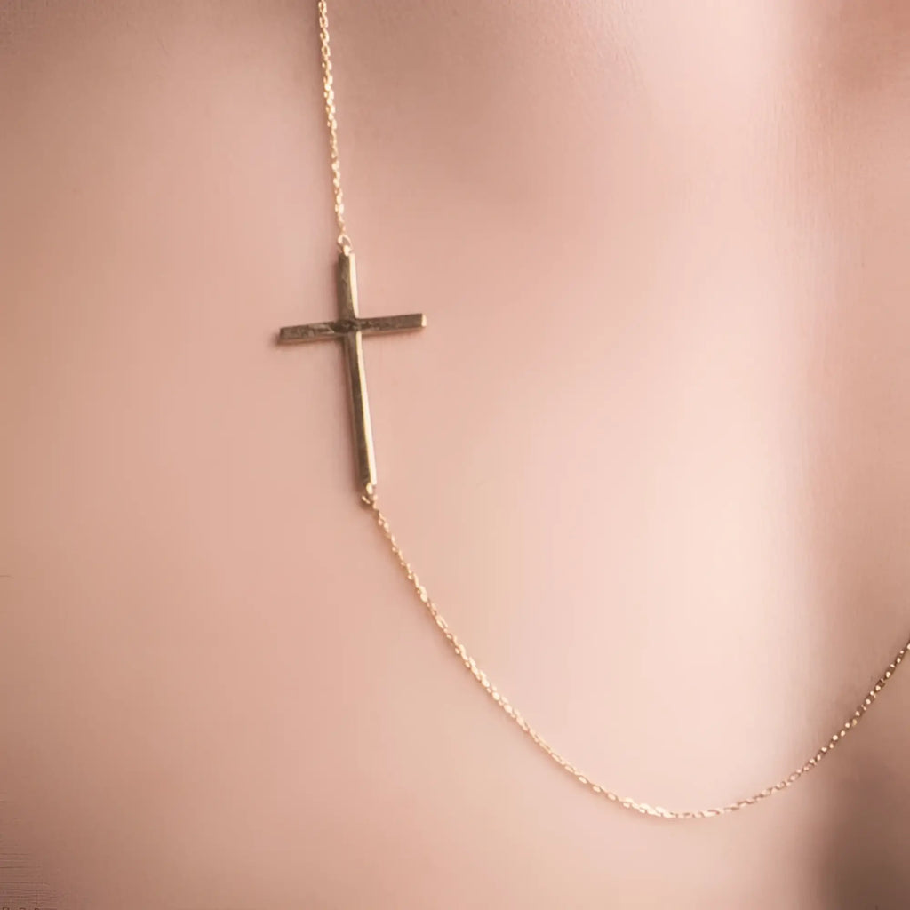 A gold-toned delicate cross necklace with a minimalist sideways design featuring slender bars and fine chain links