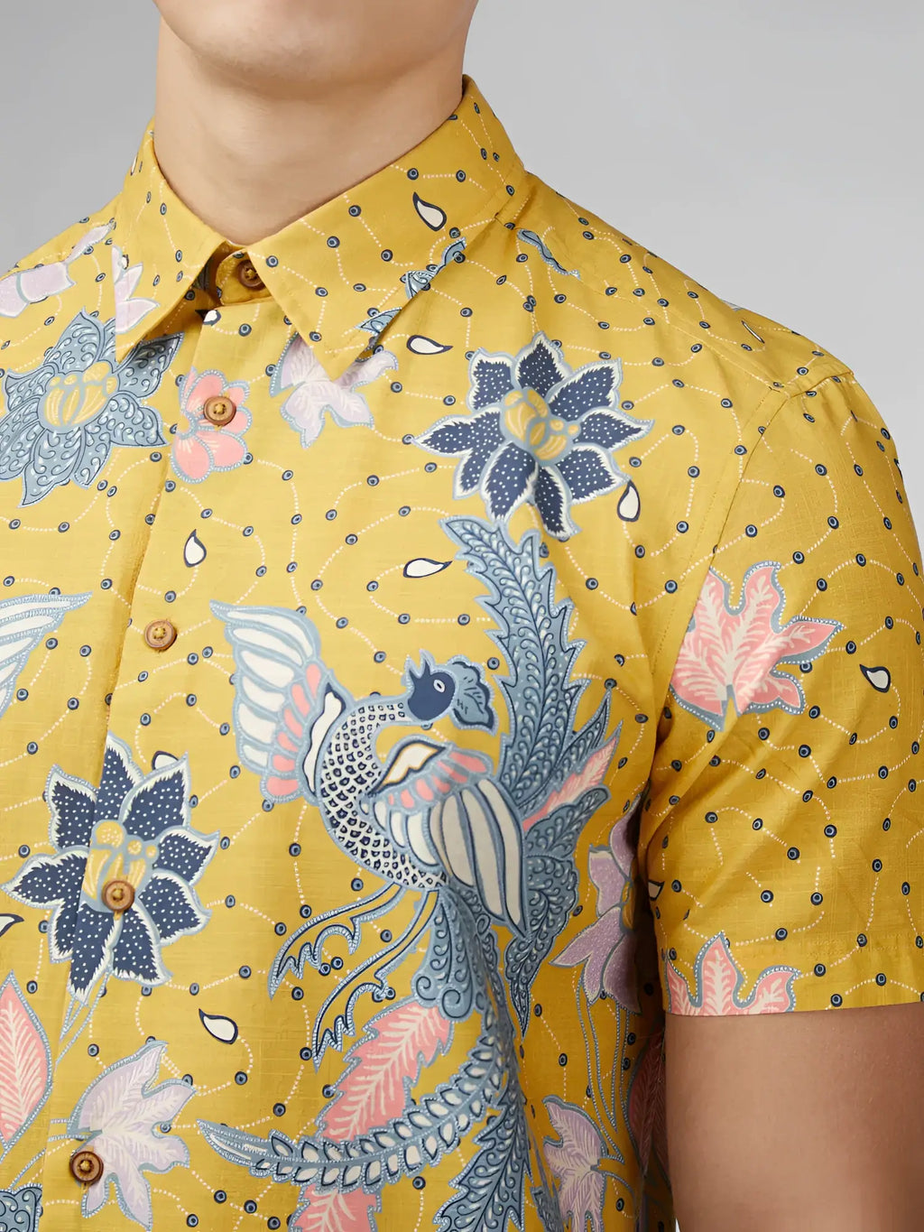 Yellow short-sleeved button-up shirt with intricate blue pink and white floral and bird patterns on textured fabric