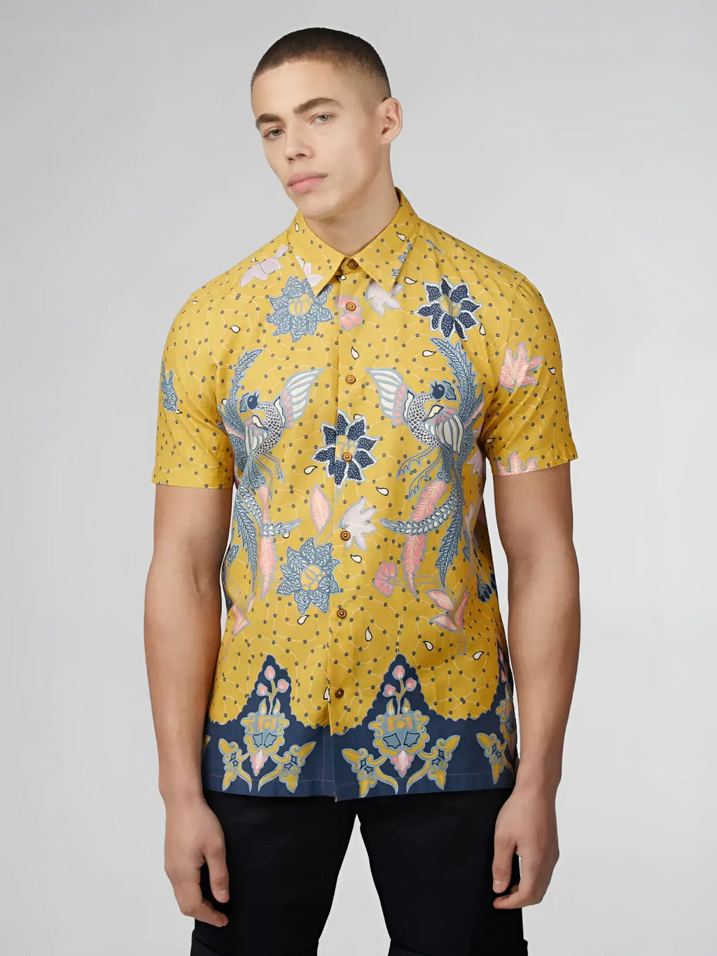 Yellow short-sleeved button-up shirt with intricate blue pink and white floral and bird patterns on dotted background