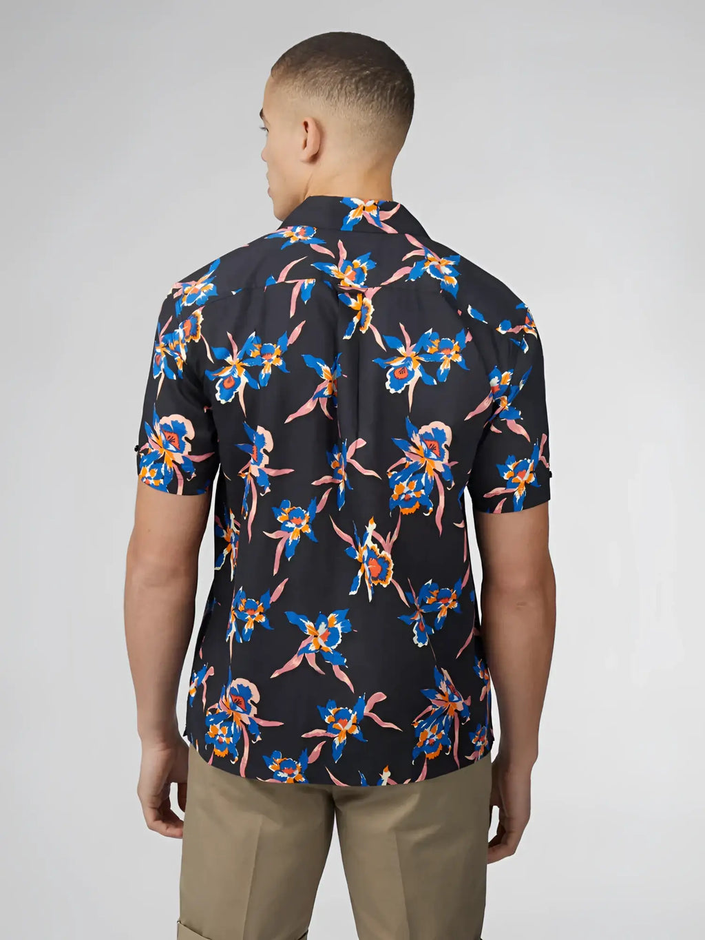 A man wearing a dark navy short-sleeved button-up shirt with vibrant blue and pink floral patterns signature botanical print