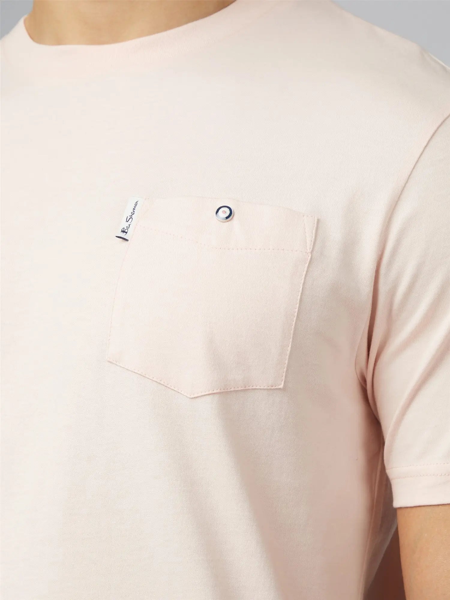 A soft blush pink signature t-shirt with short sleeves and a chest pocket featuring a silver button closure