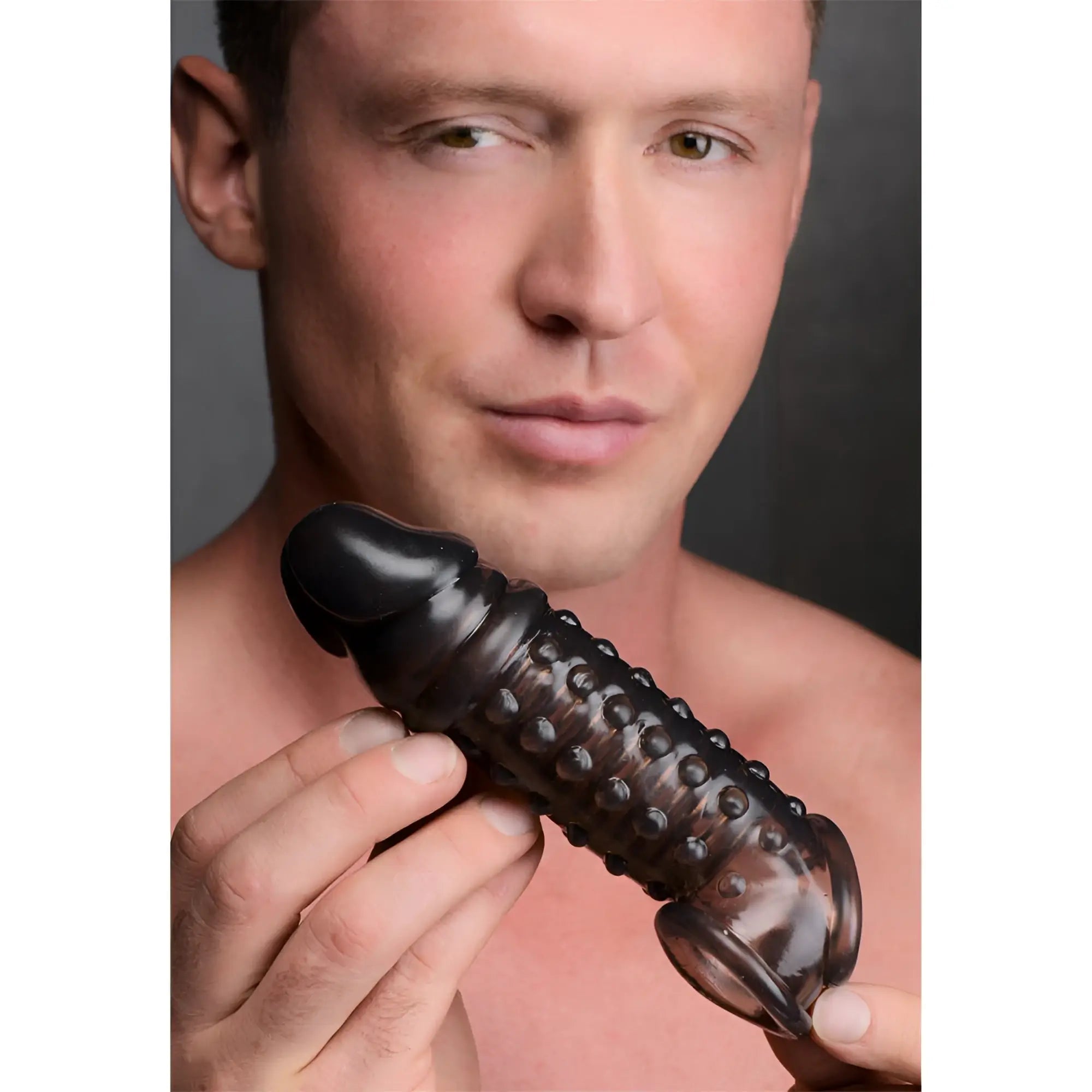 A man holding a translucent black, textured 1.5-inch Size Matters penis enhancer sleeve.