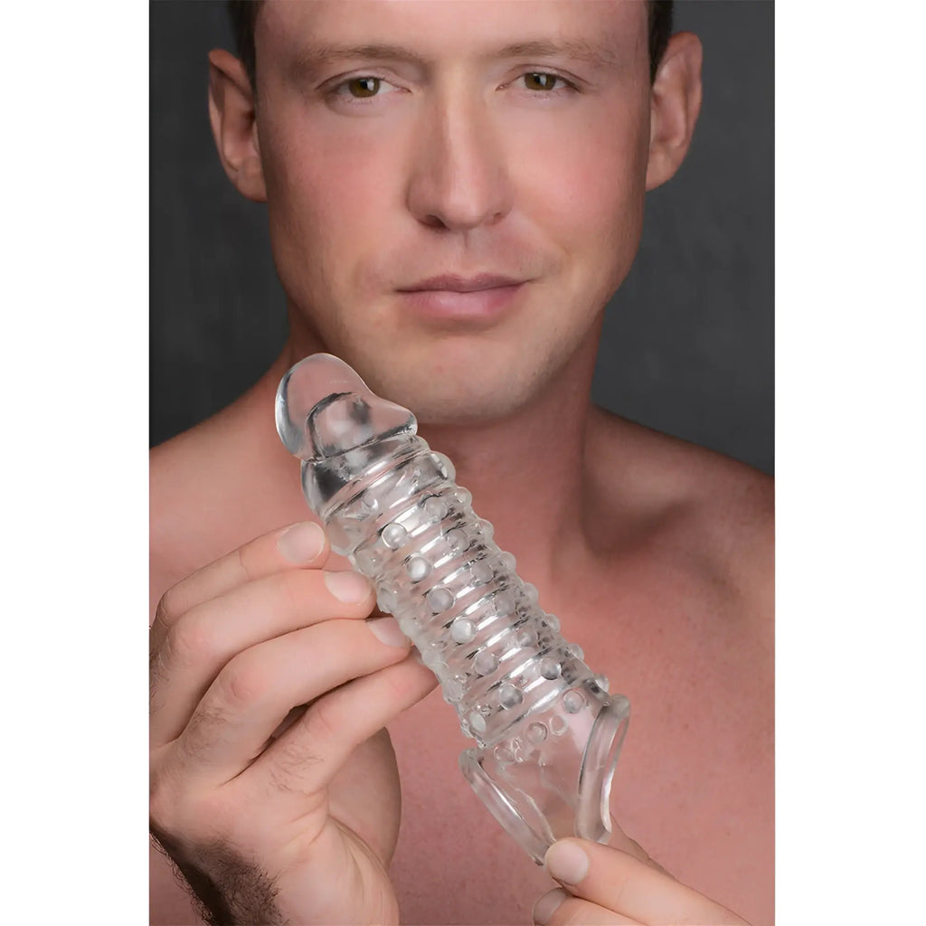 A man holding a clear, ribbed Size Matters 1.5-inch penis enhancer sleeve with a textured, studded design.