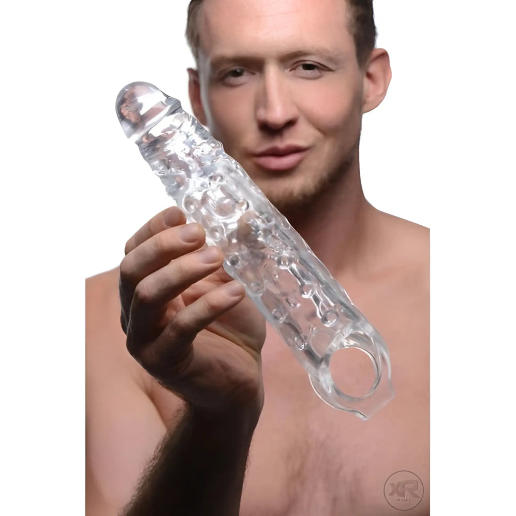 A man holds a clear, textured Size Matters 3-Inch Extender Sleeve with a rounded tip and a circular ring base.