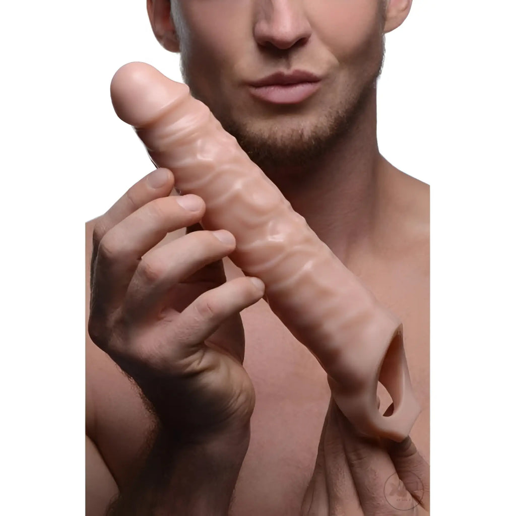 A man holds a flesh-colored, 3-inch Size Matters extender sleeve with realistic, textured, veiny detail.