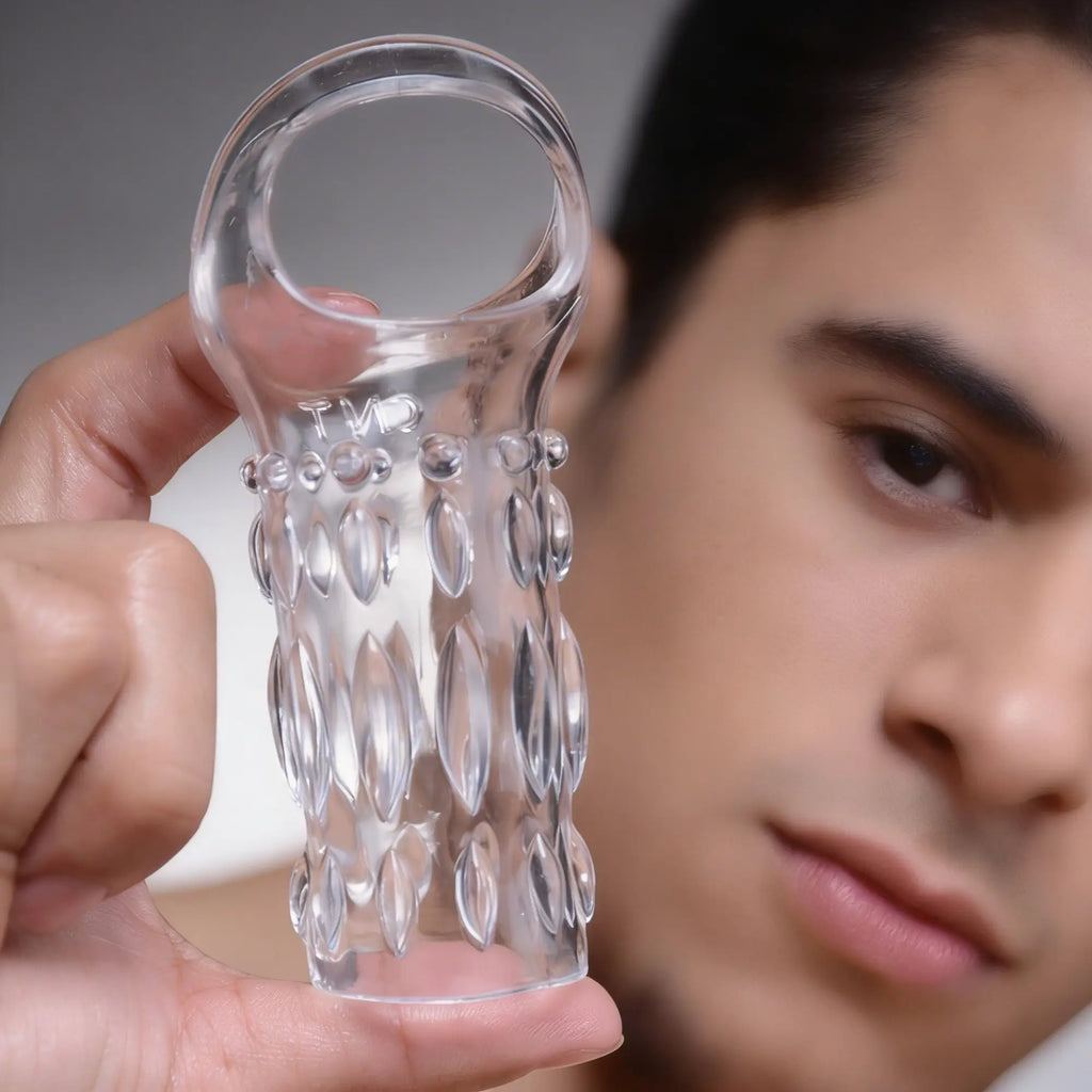A hand holds the clear, textured Size Matters Clear Sensations Enhancer Sleeve in front of a person's face.