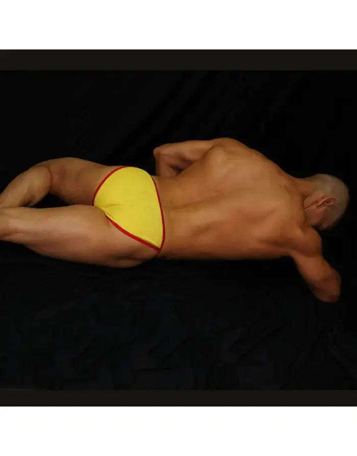 Yellow bikini underwear with red trim shown on a model lying down by Arroyman.