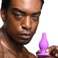 A man holding a purple Squeeze-It Squeezable Tapered Anal Plug against a white background.