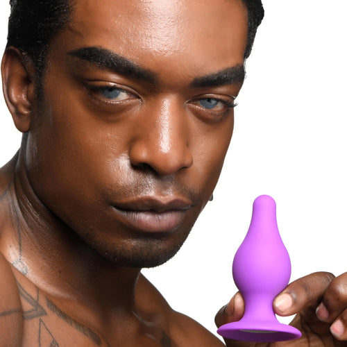 A man holding a purple Squeeze-It Squeezable Tapered Anal Plug against a white background.