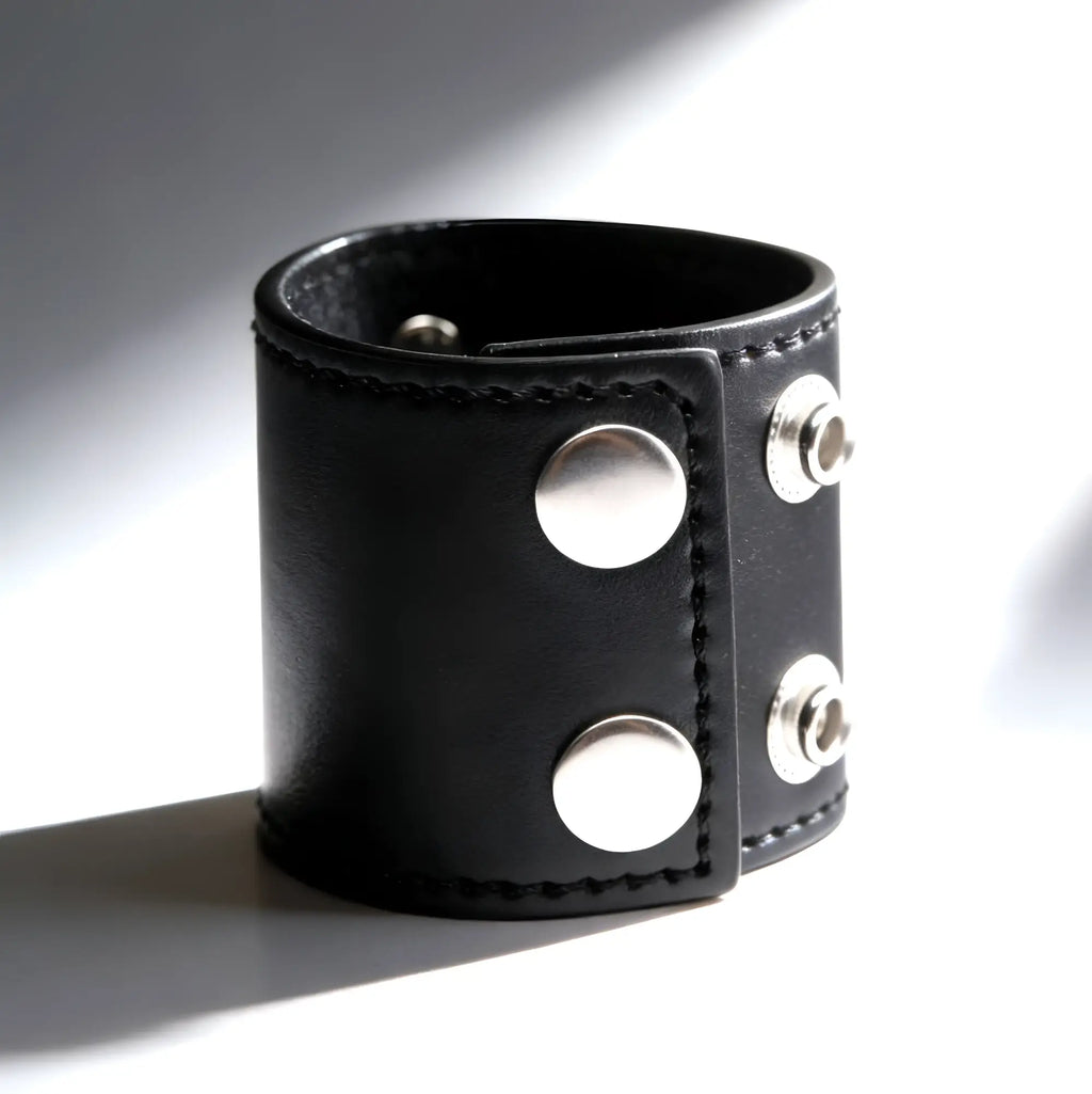 Strict 2-inch black leather ball stretcher cuff with silver-tone snap closures, shown in a studio setting.