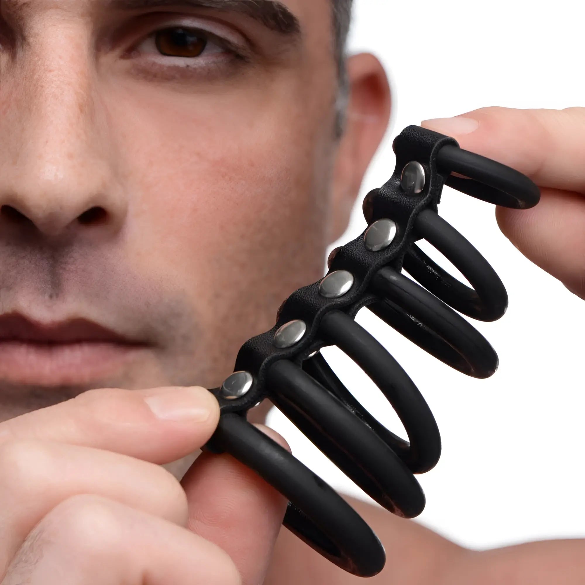 A person holding a Strict 6 Ring Silicone Chastity Cage, featuring six black silicone rings connected by silver studs.