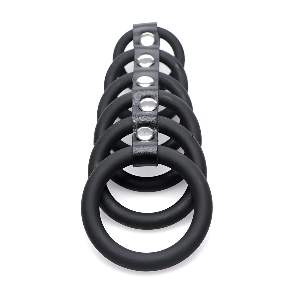 Strict 6 Ring Silicone Chastity Cage: Six black silicone rings aligned and connected by a central silver-studded strap.