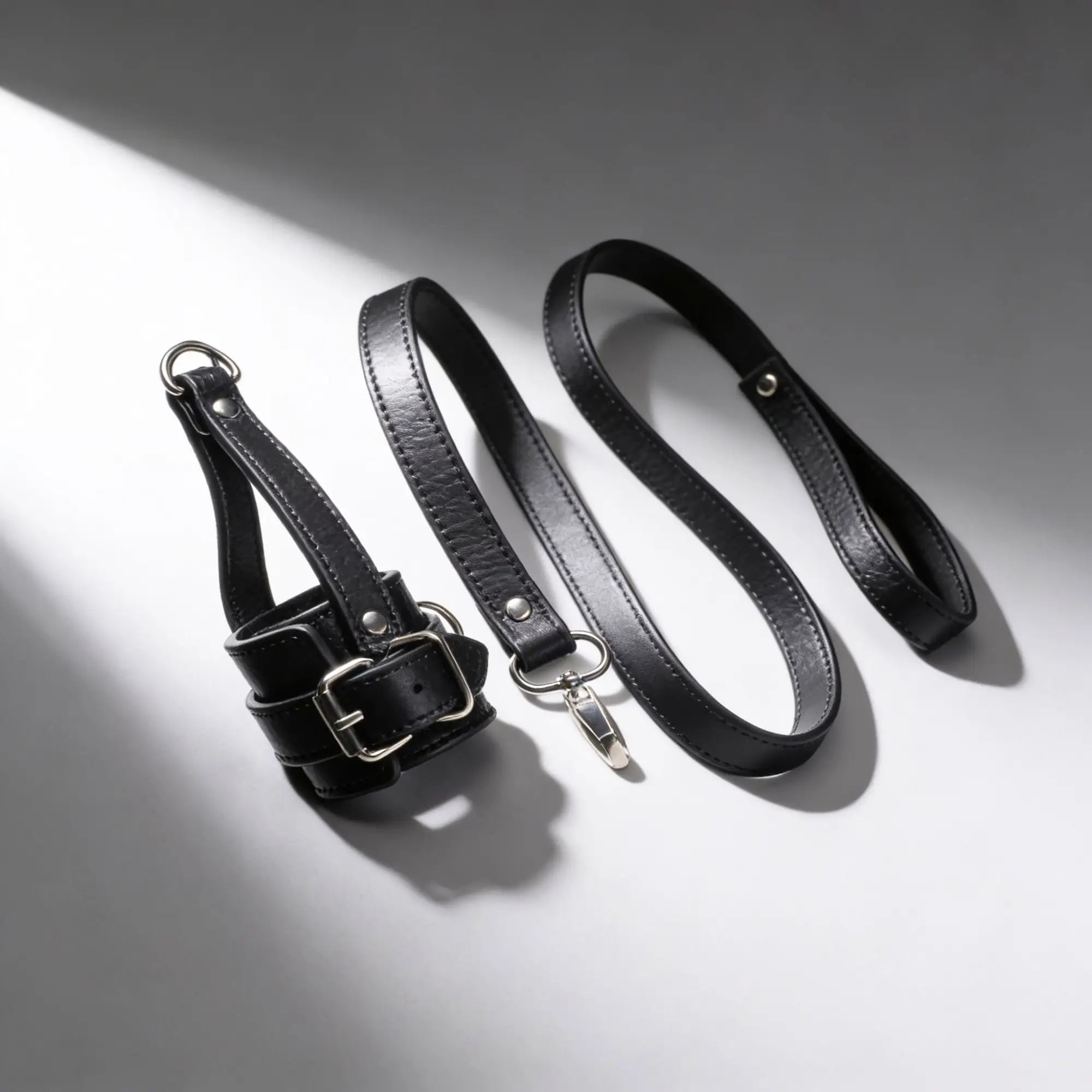 Strict Ball Stretcher with Leash: black leather restraint with silver buckle and metal snap-hook leash on white surface.
