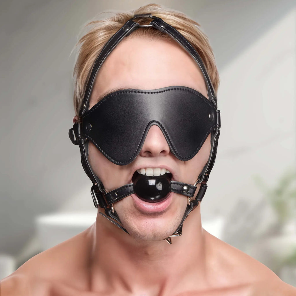 Strict Blindfold Harness and Ball Gag: A person wears a black leather blindfold, adjustable head harness, and ball gag.