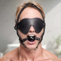 Strict Blindfold Harness and Ball Gag: A person wears a black leather blindfold, adjustable head harness, and ball gag.